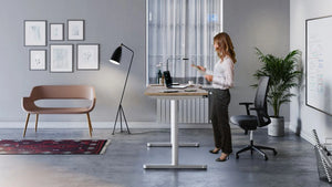 RoundE Bamboo Sit Stand Desk in White Leg Finish with Black Mesh Back Armchair and Brown Sofa in Modern Office Setting